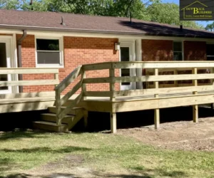 view of the completed elevated wooden deck installation wrapping along the rear exterior of the brick house under a clear blue sky, referencing custom deck services