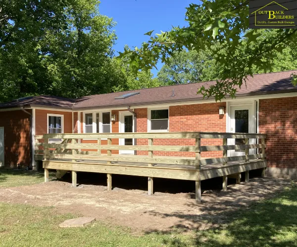 view of the completed elevated wooden deck installation wrapping along the rear exterior of the brick house under a clear blue sky, referencing custom deck services
